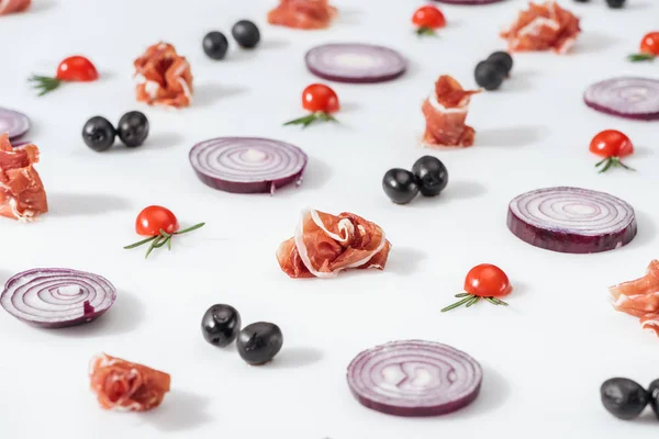 Selective focus of red onions near prosciutto and cherry tomatoes with rosemary twigs on white background — Stock Photo