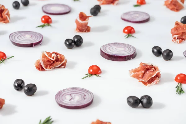 Selective focus of red onions near prosciutto, cherry tomatoes with rosemary twigs and black olives  on white background — Stock Photo