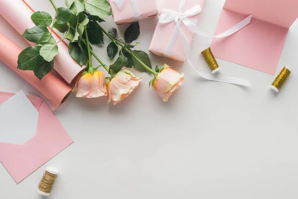 Ansicht von rosa Rosen, Papierrollen, verpackten Geschenken und Umschlägen auf grauem Hintergrund — Stockfoto