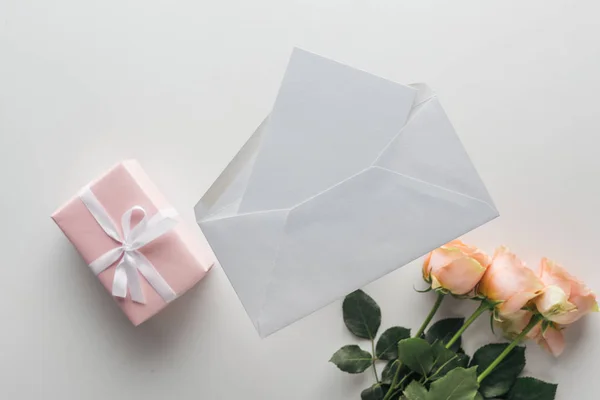 Top view of pink roses, wrapped gifts, envelope and card on grey background — Stock Photo