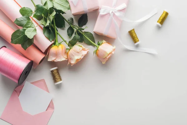 Ansicht von Rosen, Papierrollen, verpackten Geschenken, Umschlägen, Grußkarten und Garnrollen auf grauem Hintergrund — Stockfoto