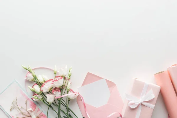 Vista dall'alto di eustoma rosa, rotoli di carta, regali avvolti, busta e biglietto di auguri su sfondo grigio — Foto stock