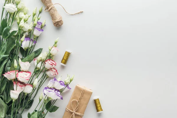 Draufsicht auf Eustoma, verpacktes Geschenk, Garn und Garnspulen auf grauem Hintergrund — Stockfoto