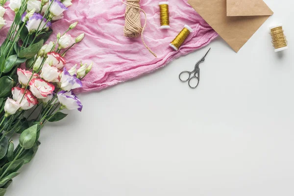 Top view of eustoma, envelopes, spools of thread, scissors and cloth on grey background — Stock Photo