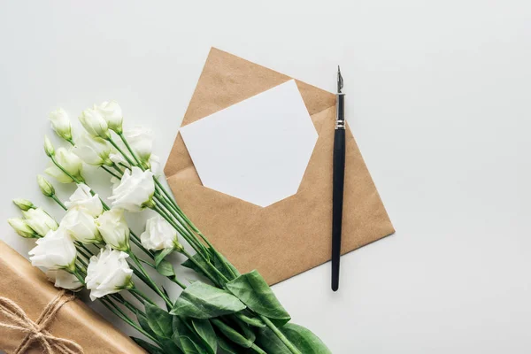 Вид зверху на еустому, загорнутий подарунок, конверт з порожньою карткою та чорниловою ручкою на сірому фоні — стокове фото