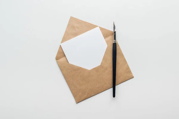 Вид зверху на коричневий конверт з порожньою карткою та чорнильною ручкою на сірому фоні — стокове фото