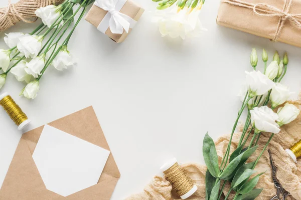 Вид сверху на цветы, завернутые подарки, конверт с пустой картой и тканью на сером фоне — стоковое фото