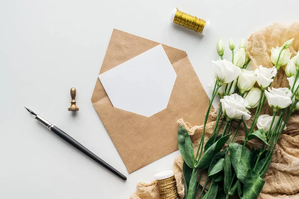 Top view of eustoma, envelope with empty card, cloth and ink pen on grey background — Stock Photo