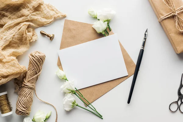 Vue de dessus des fleurs, tissu, timbre, enveloppe avec carte vide et stylo encre sur fond gris — Photo de stock