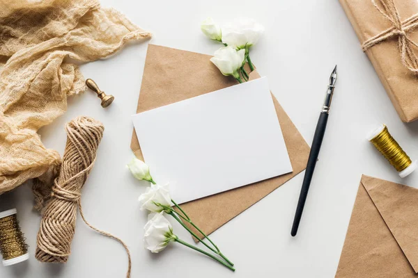 Top view of eustoma, cloth, stamp, envelope with empty card and ink pen on grey background — Stock Photo