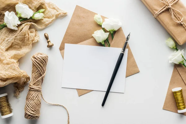 Vista dall'alto della busta con carta vuota e penna inchiostro, fiori, stoffa, timbro, regalo avvolto su sfondo grigio — Foto stock