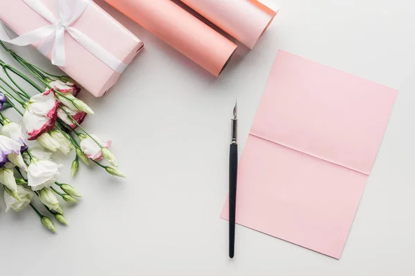 Top view of pink empty card with ink pen, flowers and rolls of paper on grey background — Stock Photo