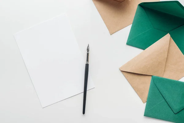 Top view of empty card with black ink pen, brown and green envelopes on grey background — Stock Photo