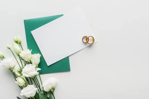 Vista superior do cartão vazio com envelope verde, flores e anéis de casamento dourados no fundo cinza — Fotografia de Stock