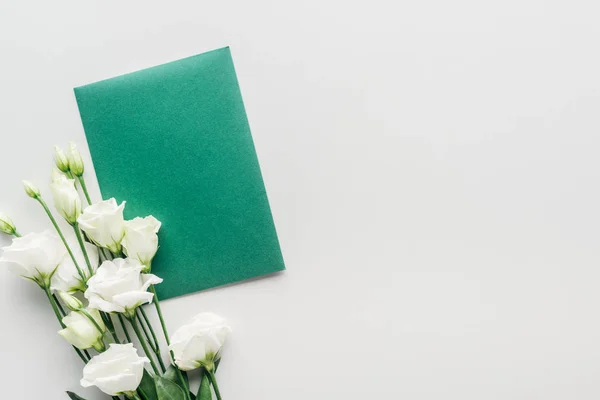 Draufsicht auf leeren grünen Umschlag mit Blumen auf grauem Hintergrund — Stockfoto