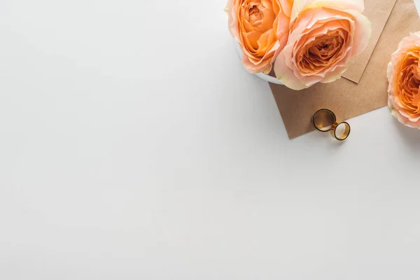 Top view of brown envelope, flowers and golden wedding rings on grey background — Stock Photo