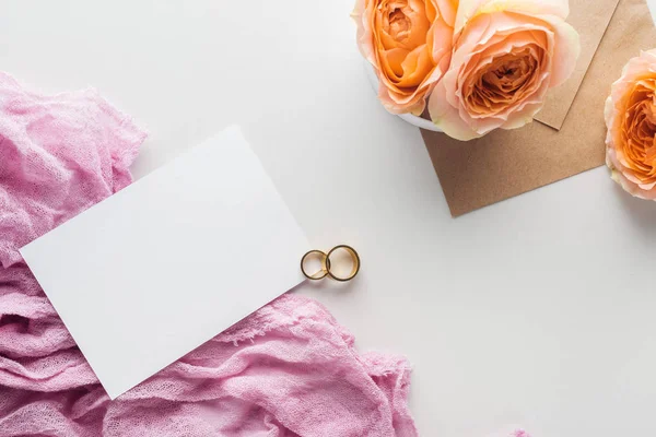 Top view of empty card, envelope, flowers, cloth and golden wedding rings on grey background — Stock Photo