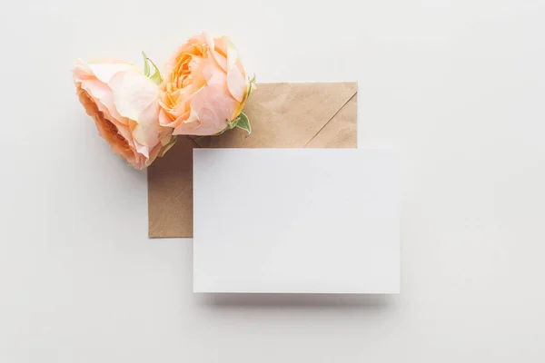 Top view of empty blank over brown envelope and pink roses on grey background — Stock Photo