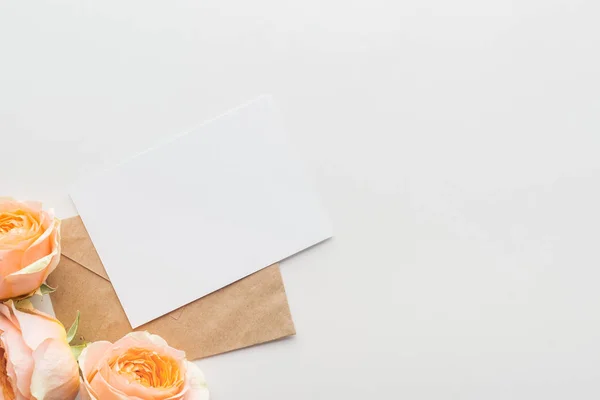 Draufsicht auf leeren Rohling mit braunem Umschlag und rosa Rosen auf grauem Hintergrund — Stockfoto