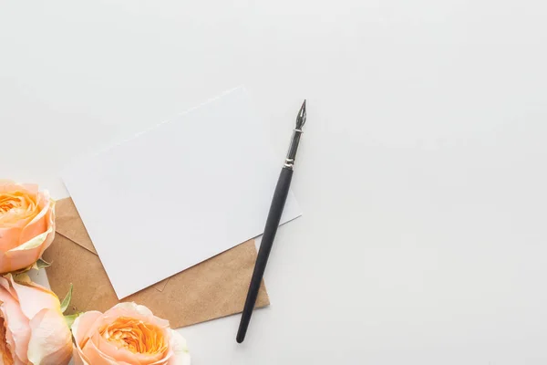 Draufsicht auf leeren Rohling mit braunem Umschlag, Federhalter und rosa Rosen auf grauem Hintergrund — Stockfoto