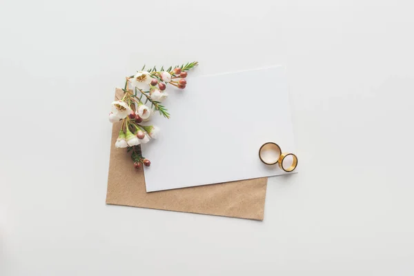 Top view of empty card with brown craft paper envelope and wedding rings on grey background — Stock Photo