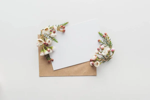 Draufsicht auf leeren Rohling mit braunem Umschlag und Blumen auf grauem Hintergrund — Stockfoto