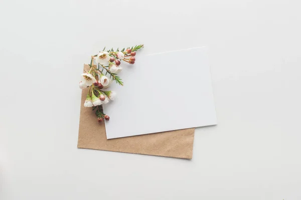Vista superior de vazio em branco com envelope de papel artesanal marrom e flores em fundo cinza — Fotografia de Stock