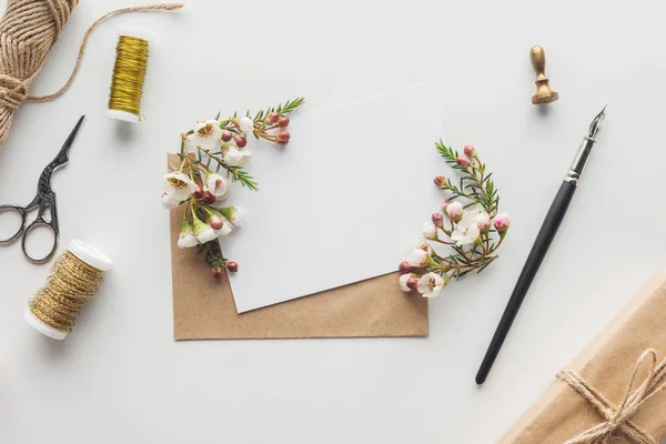 Vista dall'alto di vuoto vuoto con busta marrone, penna inchiostro, fiori, forbici, timbro, bobine di filo e regalo avvolto su sfondo grigio — Foto stock