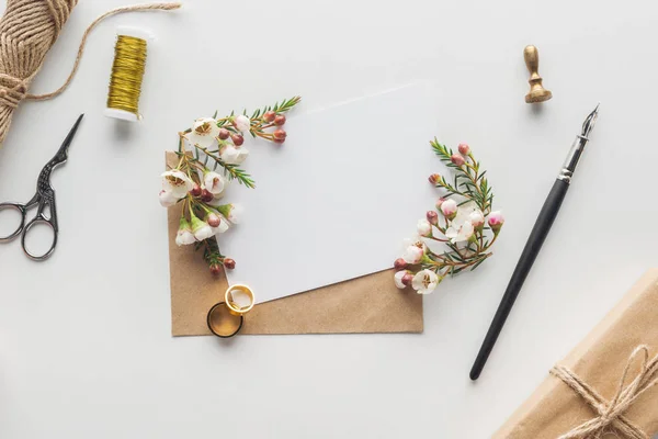 Top view of empty card with envelope, ink pen, flowers, wrapped gift, stamp, scissors, spool of thread and wedding rings on grey background — Stock Photo