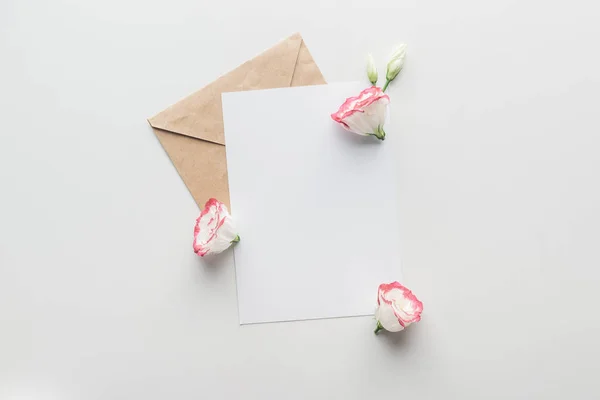 Top view of empty blank with brown craft paper envelope and eustoma on grey background — Stock Photo