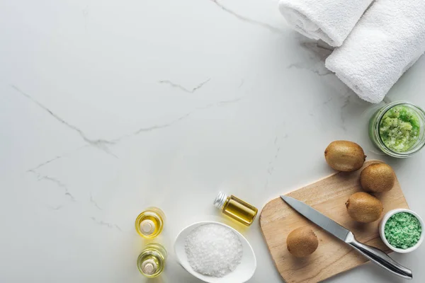 Draufsicht auf Schneidetisch mit geschnittener Kiwi und verschiedenen natürlichen Komponenten für hausgemachte Kosmetik auf weißer Oberfläche — Stockfoto