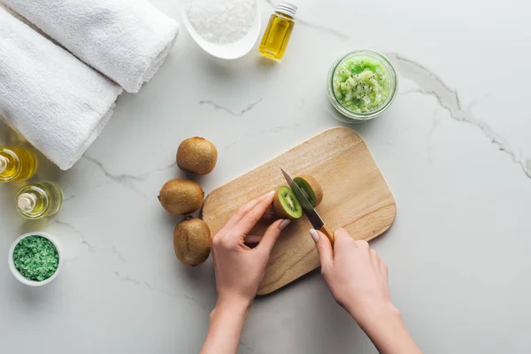 Cropped view of woman cutting kiwi on wooden cutting desk on white surface — Stock Photo