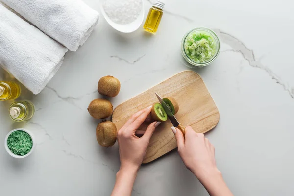 Abgeschnittene Ansicht einer Kiwi schneidenden Frau auf einem hölzernen Schneidetisch auf weißer Oberfläche — Stockfoto