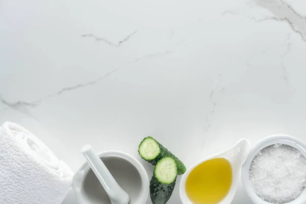 Top view of bowls with oil and salt, cucumber halves, pounder and towel on white surface — Stock Photo