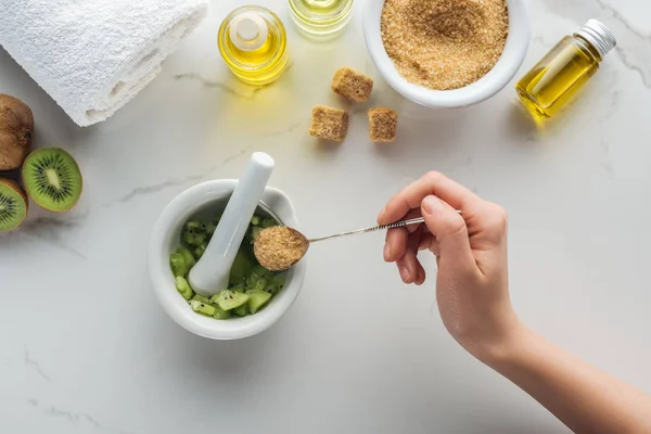 Cropped view of woman adding brown sugar into pounder with kiwi on white surface — Stock Photo
