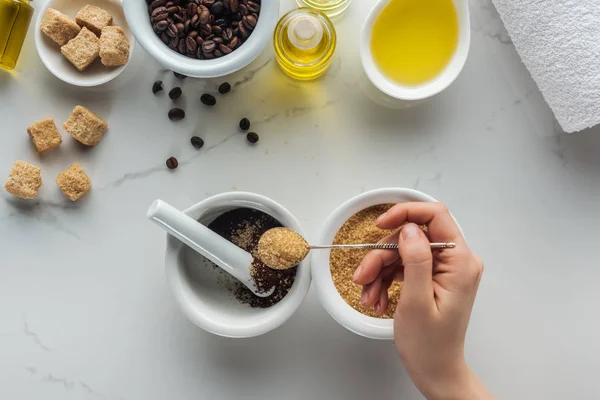 Partial view of woman adding brown sugar into pounder with ground coffee on white surface — Stock Photo