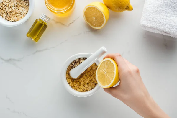 Partial view of female hand with half lemon, and pounder with mixed oat flakes and honey on white surface — Stock Photo