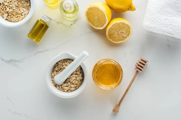 Top view of pounder with oat flakes, bowl with honey, lemons and various components on white surface — Stock Photo
