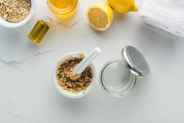 Top view of pounder with mixed oat flakes and honey, empty glass container, and various natural ingredients on white surface — Stock Photo