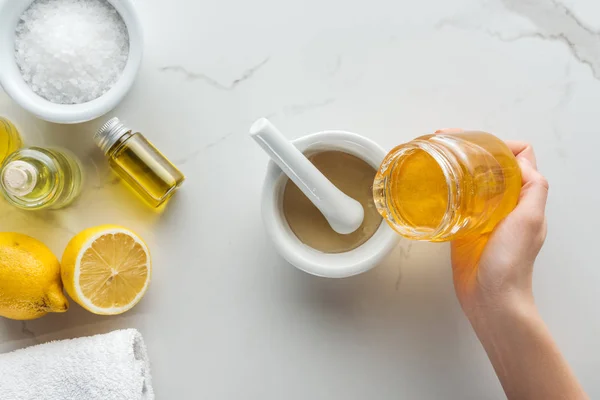 Vista ritagliata di donna versando miele in libbre, e vari ingredienti naturali per cosmetici fatti a mano sulla superficie bianca — Foto stock