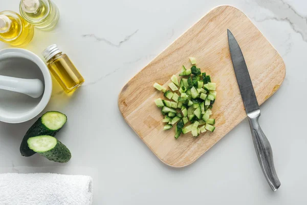 Top with of wooden cutting desk with cut cucumber cubes, and various ingredients for cosmetics making on white surface — Stock Photo