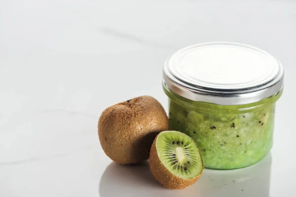 Glass container with kiwi puree, whole and half kiwi on white surface — Stock Photo