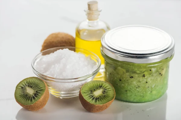 Fuoco selettivo del contenitore di vetro con purea di kiwi, ciotola di sale, bottiglia di olio e kiwi sulla superficie bianca — Foto stock