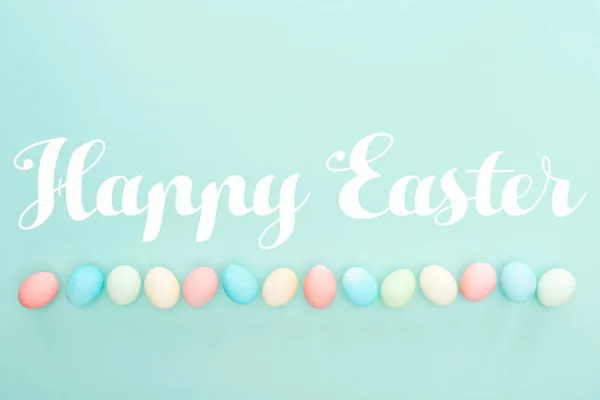 Top view of pastel painted eggs in row with Happy easter lettering isolated on blue — Stock Photo