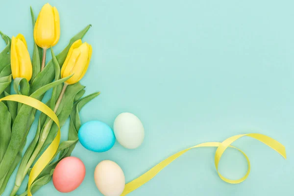 Vue du dessus des fleurs de tulipes jaunes avec ruban et oeufs de Pâques isolés sur bleu avec espace de copie — Photo de stock