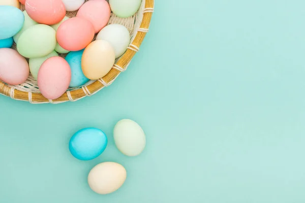 Vue de dessus des œufs de Pâques pastel traditionnels dans une assiette en osier isolée sur bleu avec espace de copie — Photo de stock