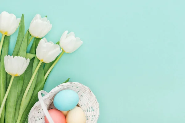 Vista superior de flores de tulipa e ovos de Páscoa em cesta de vime isolado em azul com espaço de cópia — Fotografia de Stock