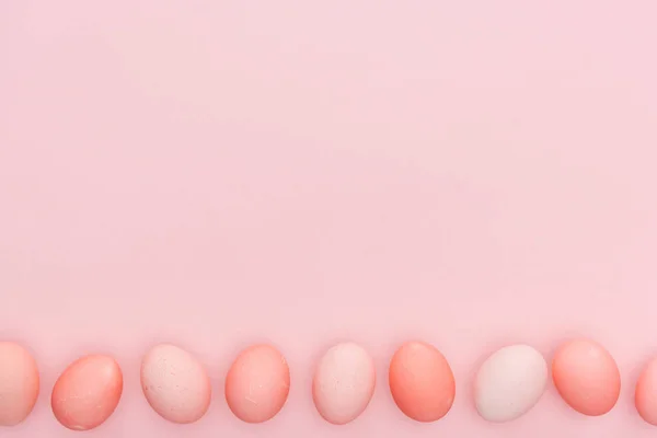 Vista dall'alto delle tradizionali uova pasquali pastello in fila isolate su rosa con spazio copia — Foto stock