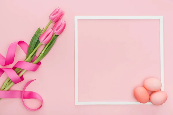 Top view of pink tulips with ribbon and easter eggs with frame isolated on pink — Stock Photo
