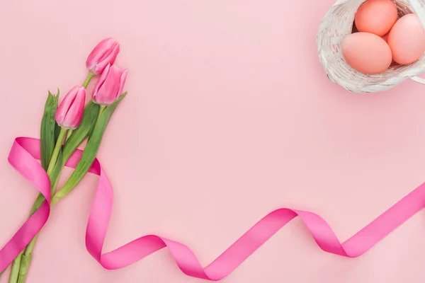 Vista dall'alto di tulipani con nastro e uova di Pasqua in cesto di vimini isolato su rosa — Foto stock